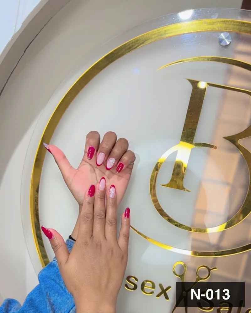 A deep red set with freehand white detail, photographed against the salon's gold monogram at Salon By Babita, Haldwani — reference N-013