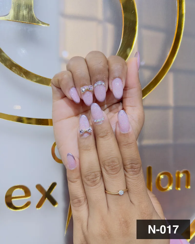 A pale pink almond set with crystal accents, photographed against the salon's gold monogram at Salon By Babita, Haldwani — reference N-017