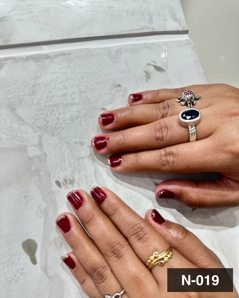 A deep wine short almond set, both hands flat on the salon's marble counter at Salon By Babita, Haldwani — reference N-019