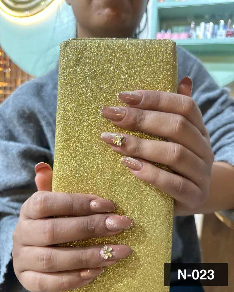 A nude ombré almond set with crystal accents, held against a gold block at Salon By Babita, Haldwani — reference N-023