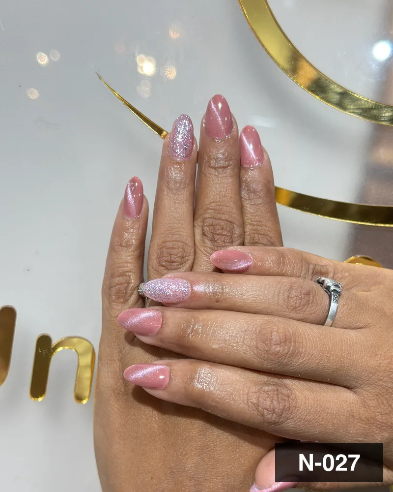 A pink glitter ombré almond set, photographed against the salon's gold monogram at Salon By Babita, Haldwani — reference N-027