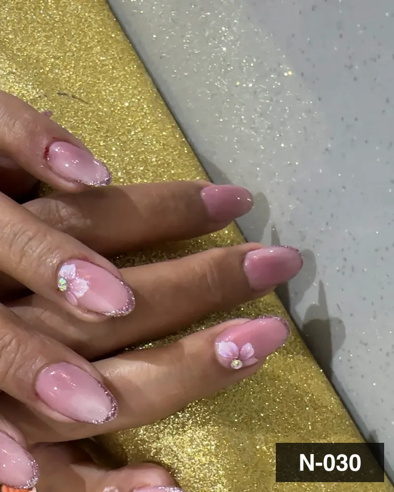 A pink ombré almond set with white flower detail, resting on a gold block at Salon By Babita, Haldwani — reference N-030
