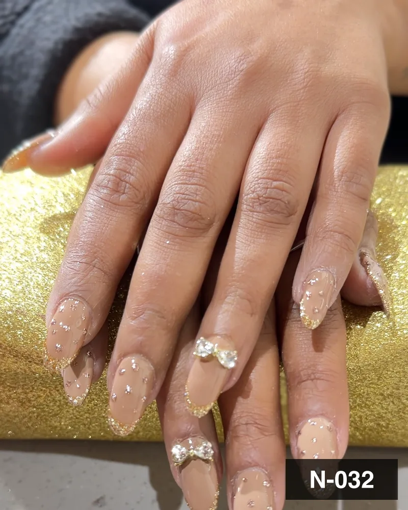 A nude glitter almond set with crystal detail, resting on a gold block at Salon By Babita, Haldwani — reference N-032