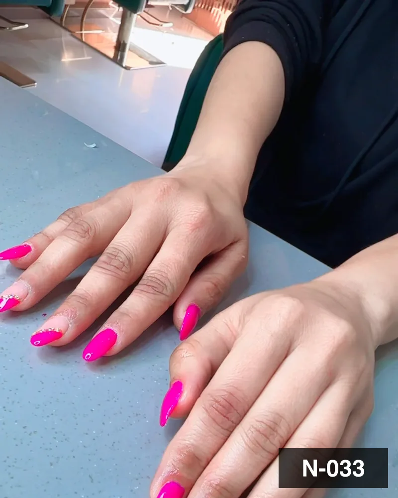A hot pink short almond set, both hands flat on the salon counter at Salon By Babita, Haldwani — reference N-033