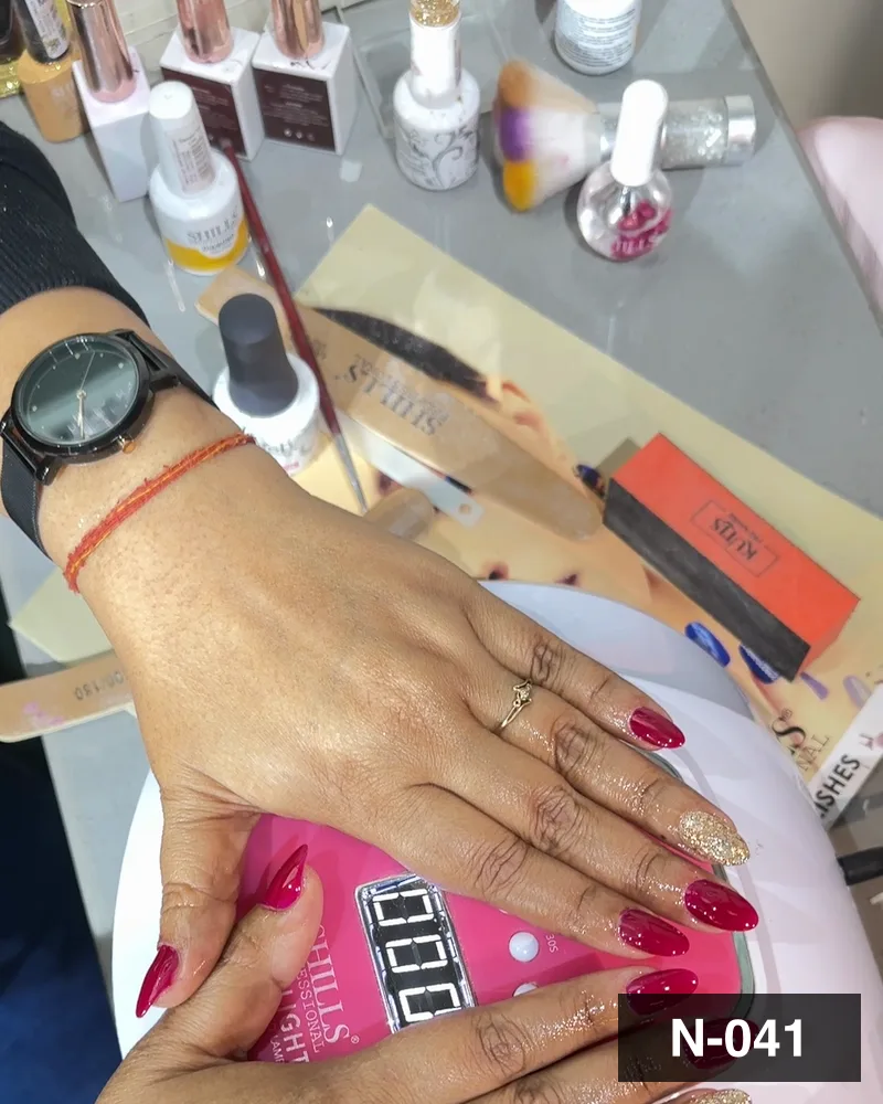 A red almond set photographed at the cure lamp on the nail table at Salon By Babita, Haldwani — reference N-041