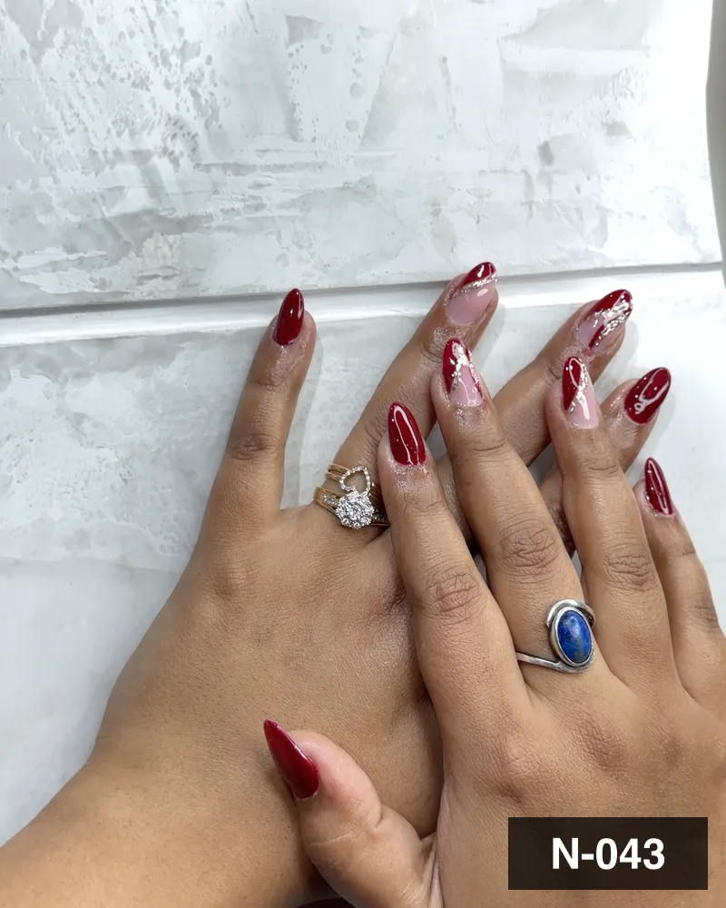 A red almond set with freehand glitter detail, photographed on the salon counter at Salon By Babita, Haldwani — reference N-043