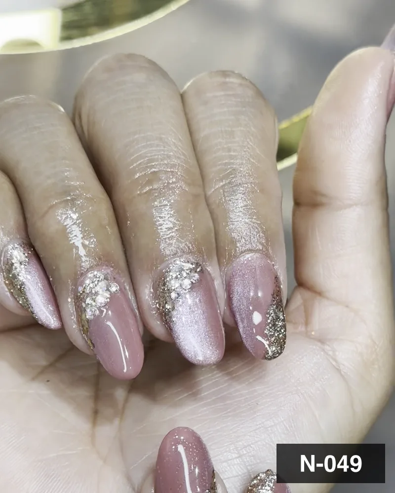 A nude and gold glitter almond set, framed close at the cuticle line at Salon By Babita, Haldwani — reference N-049
