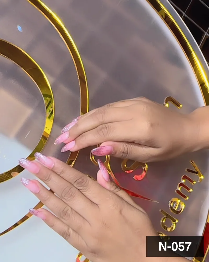 A pale pink long almond set, both hands laid on the salon's gold monogram at Salon By Babita, Haldwani — reference N-057