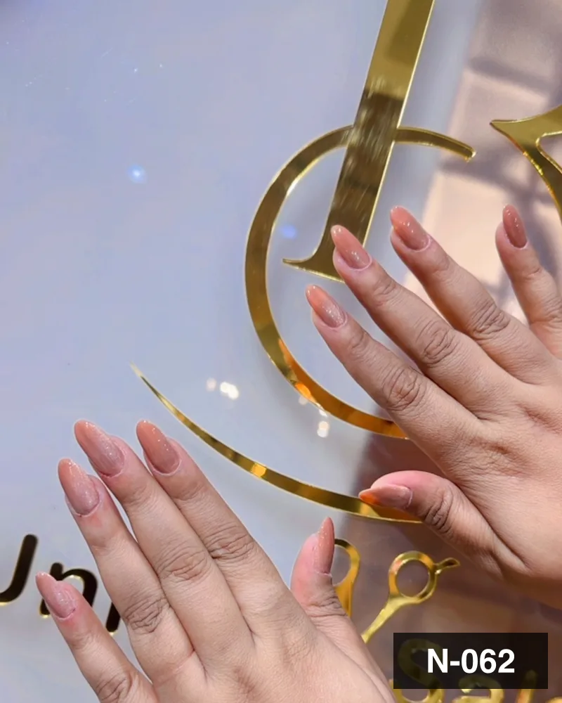 A pale nude long almond set, both hands against the salon's gold monogram at Salon By Babita, Haldwani — reference N-062