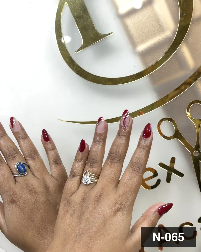 A deep red almond set with freehand art, both hands on the salon's gold monogram at Salon By Babita, Haldwani — reference N-065