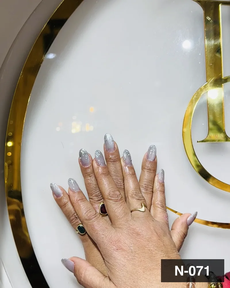 A silver glitter ombré almond set, one hand laid on the salon's gold monogram at Salon By Babita, Haldwani — reference N-071