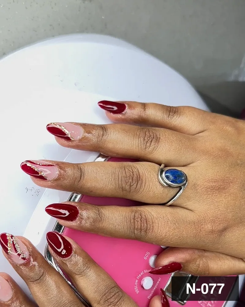 A deep red set with freehand detail, photographed at the cure lamp at Salon By Babita, Haldwani — reference N-077