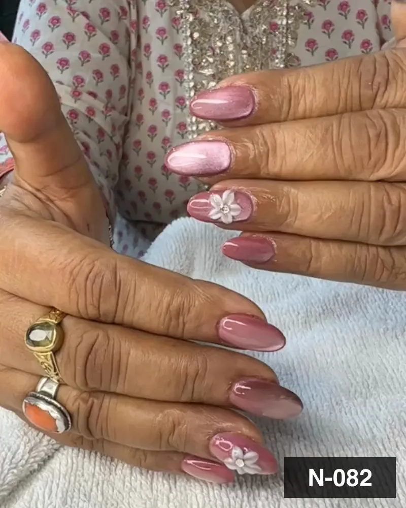 A blush pink chrome almond nail set with white 3D flower accents on both hands at Salon By Babita, Haldwani — reference N-082