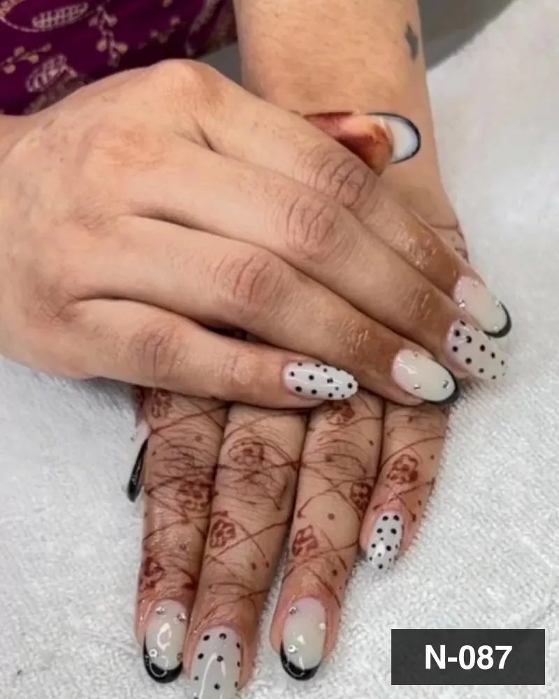 A white nail set with hand-placed black dots and a black french edge on henna-stained hands at Salon By Babita, Haldwani — reference N-087
