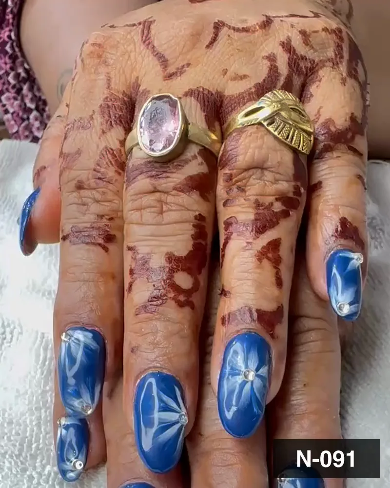 A blue and white marble long almond nail set with crystal accents on henna-stained hands at Salon By Babita, Haldwani — reference N-091