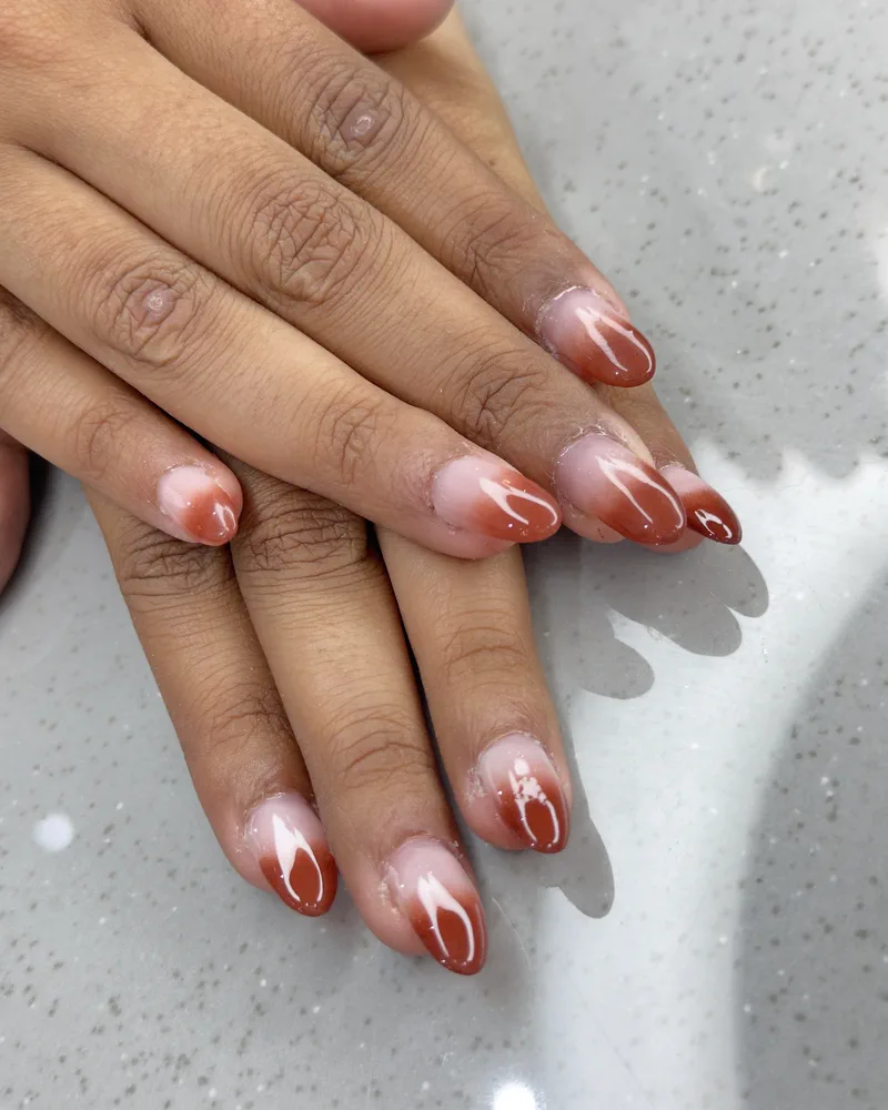 Almond-shaped nails in a red and nude ombré, photographed on the counter at Salon By Babita, Haldwani