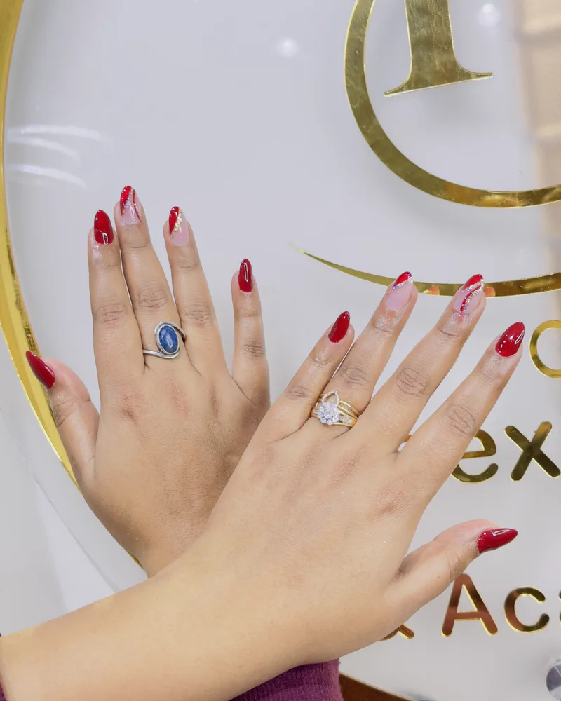 Red nails with hand-painted nail art, photographed against the salon's gold monogram at Salon By Babita, Haldwani